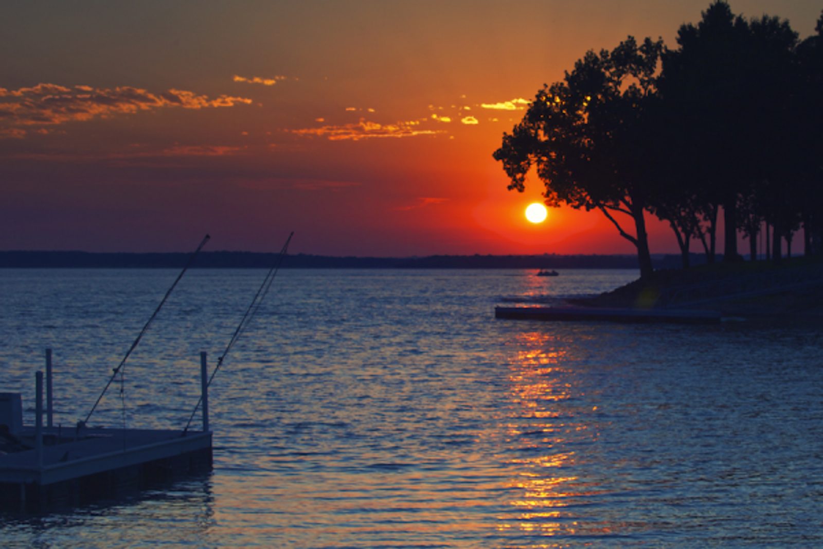 Grand Lake O' the Cherokees at sunset — fishing rods on a dock silhouetted against the sky, a tree-lined shore in the distance, Oklahoma